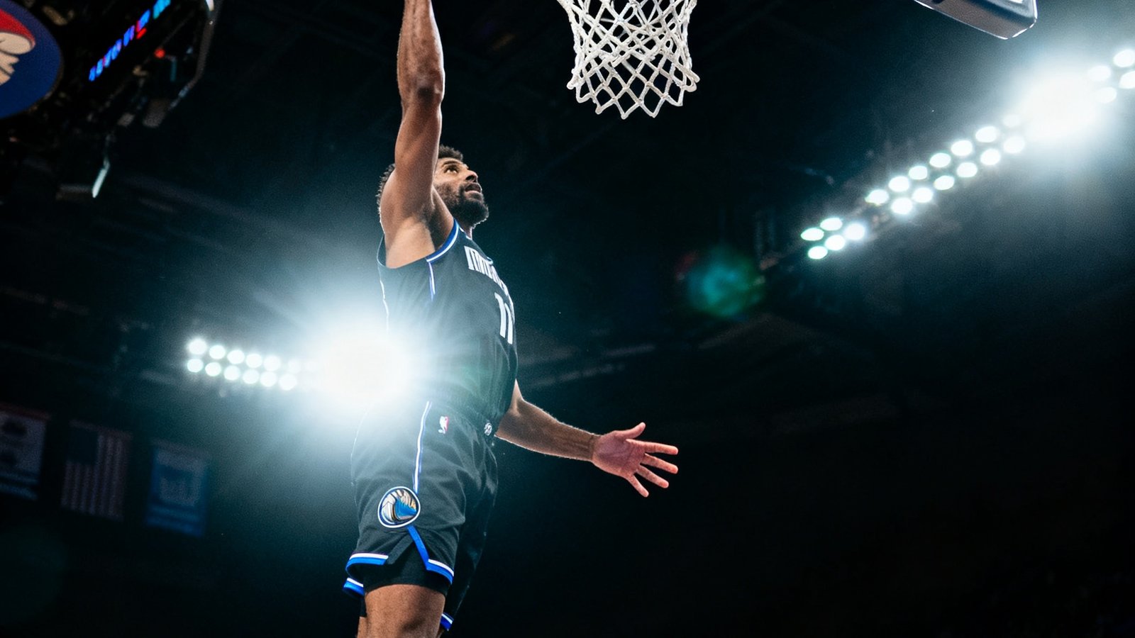 NBA篮球馆内一名球员正在投篮的瞬间，背景电子记分牌显示着实时数据，球场灯光聚焦在运动员身上